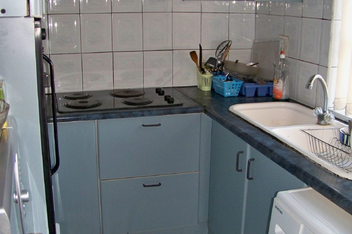 A compact, dated kitchen featuring blue cabinetry, a tiled backsplash, electric hob with extractor, and integrated sink area with tiled flooring.