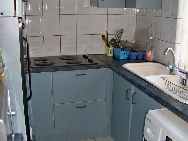 A compact, dated kitchen featuring blue cabinetry, a tiled backsplash, electric hob with extractor, and integrated sink area with tiled flooring.