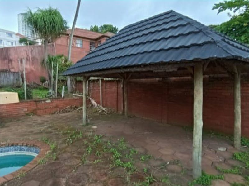Outdoor patio area featuring a gazebo structure, brick boundary walls, and an adjacent swimming pool, requiring maintenance and landscaping.