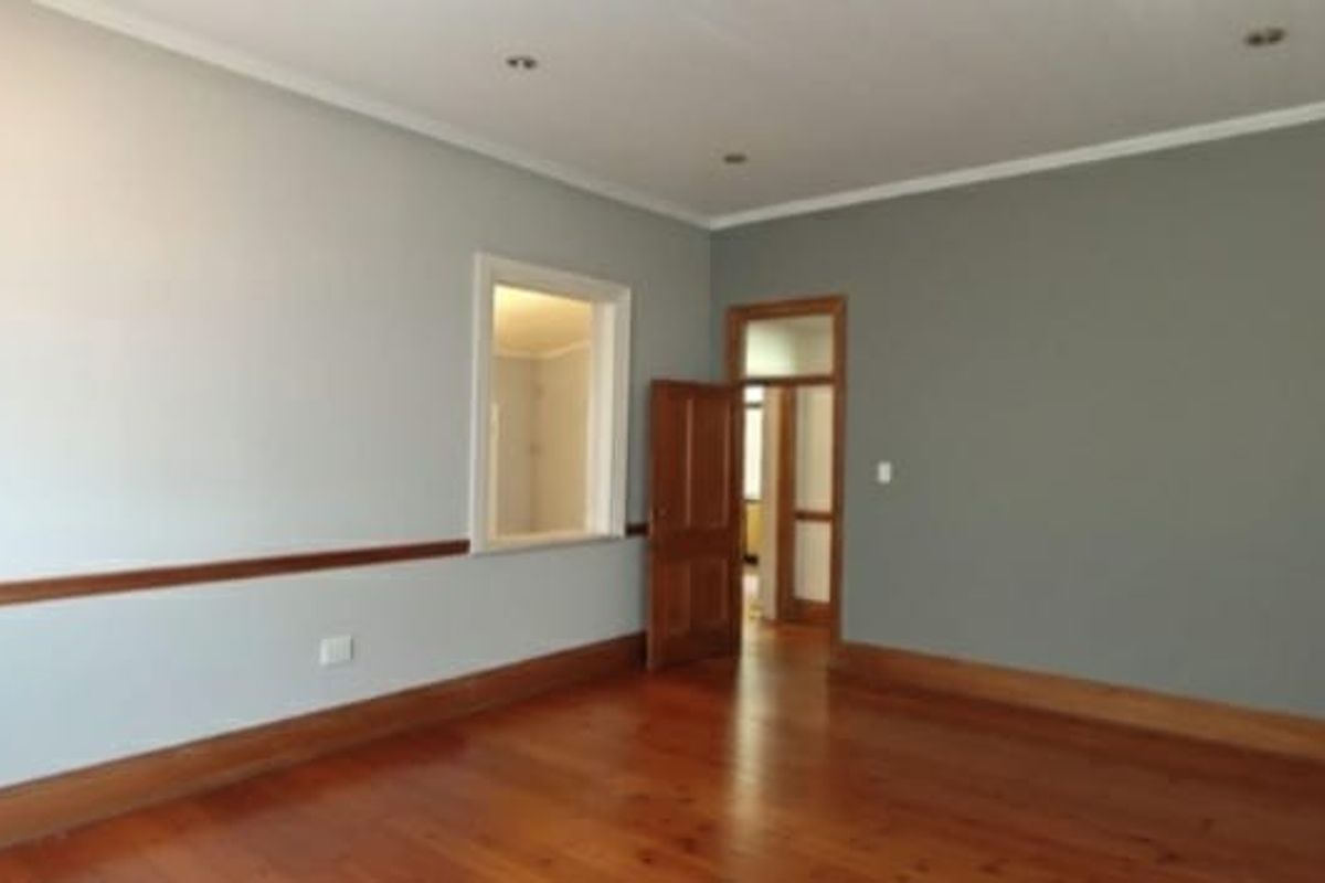A bright, empty living room featuring polished timber flooring, classic timber dado rails, and recessed downlighting, offering a clean and neutral canvas.