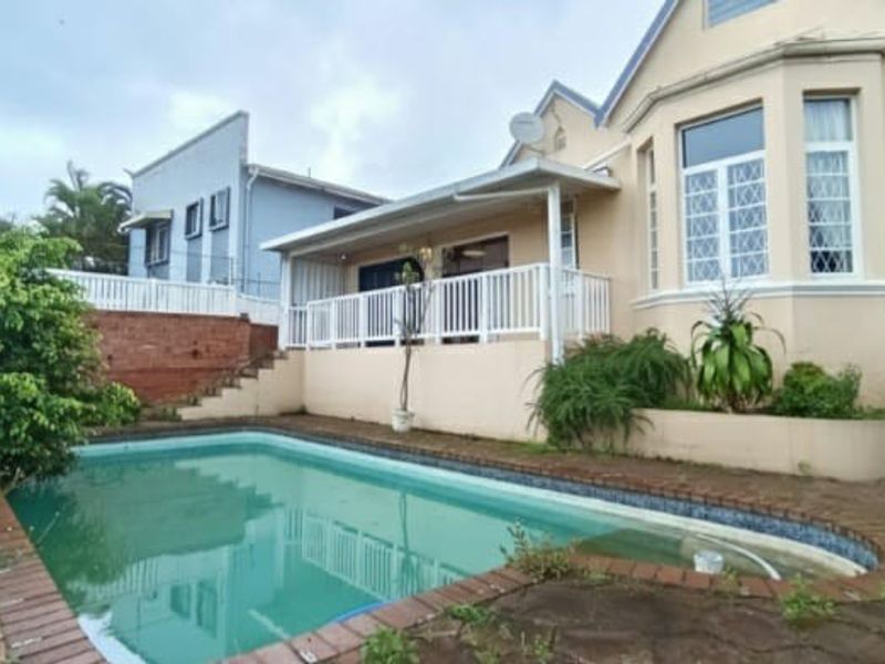 Rear exterior view featuring a swimming pool, raised patio with white balustrade, and brick paved surround.