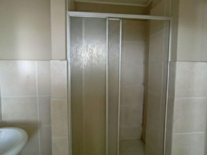 A functional bathroom featuring a shower enclosure with sliding doors and a pedestal basin with neutral wall tiling.