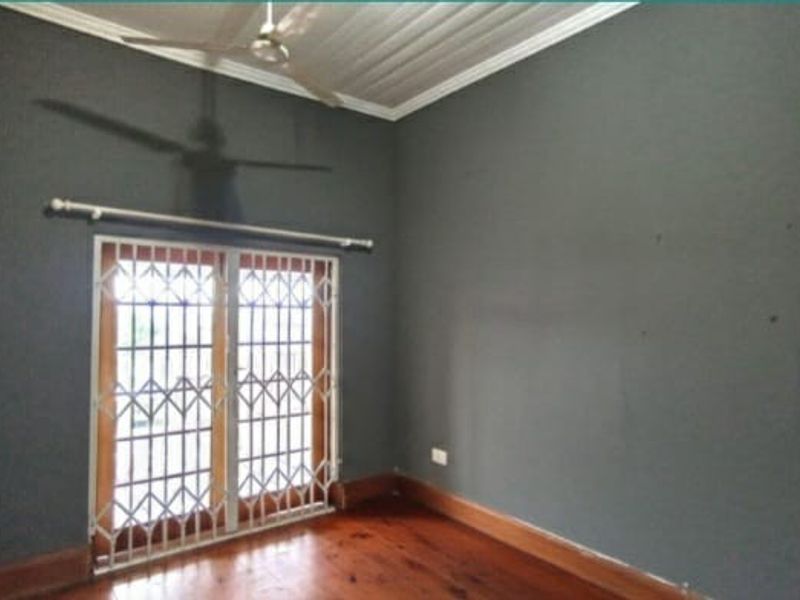 An empty bedroom featuring polished timber flooring, built-in cupboards, a ceiling fan, and a security gate over the door.