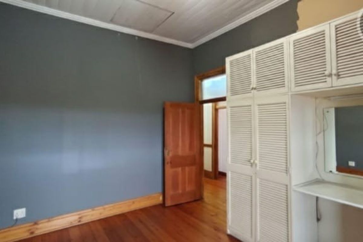 A bedroom featuring timber flooring, built-in cupboards with a vanity area, and a timber door. The room requires minor finishing touches to the walls.
