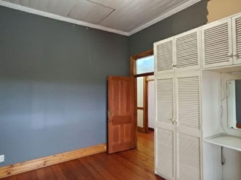 A bedroom featuring timber flooring, built-in cupboards with a vanity area, and a timber door. The room requires minor finishing touches to the walls.