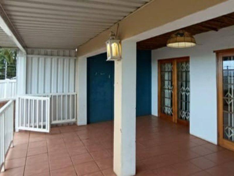 A spacious covered patio featuring tiled flooring, white metal balustrades, and timber-framed doors with security gates, offering a functional outdoor entertainment area.