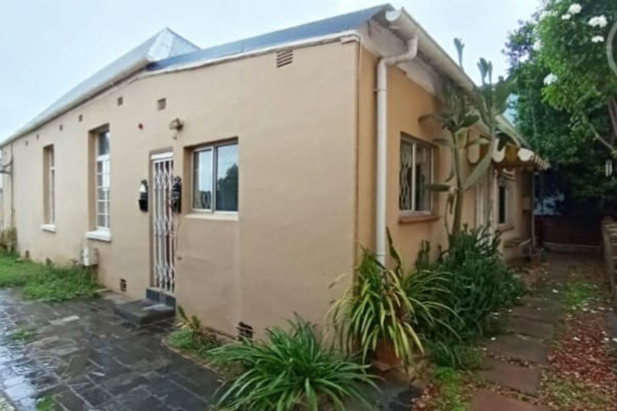 Rear exterior view of the property featuring paved pathways, security gates, and established garden surroundings.