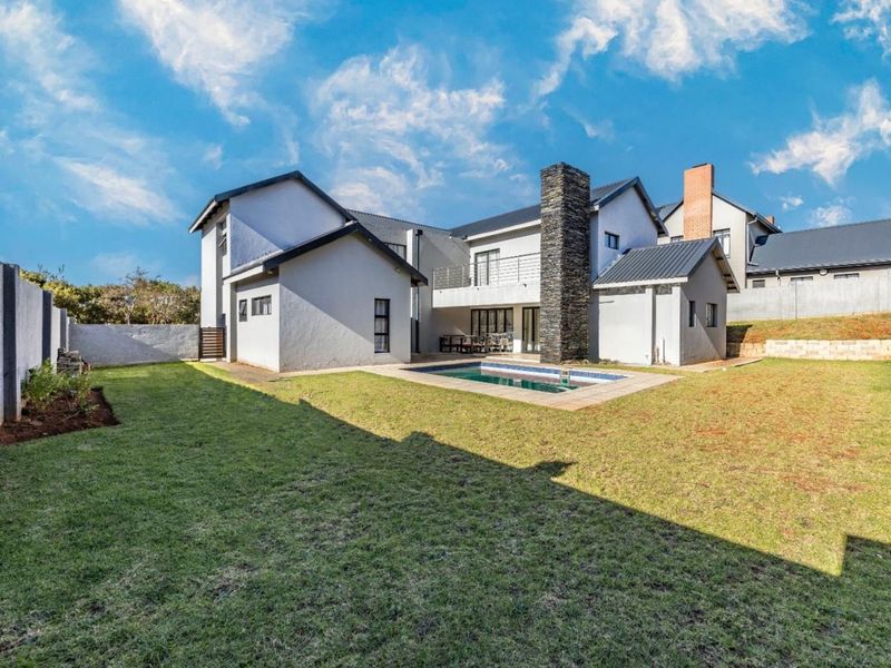 Rear view of a modern double-story house featuring a swimming pool, stone-clad chimney, and a spacious lawn area.