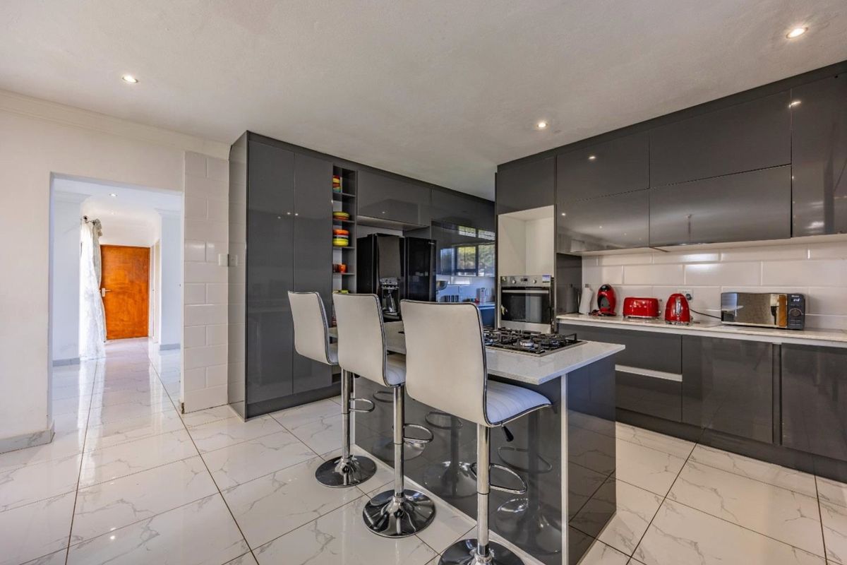 Modern kitchen featuring high-gloss grey cabinetry, a central island with a gas hob, stone countertops, and polished marble-look floor tiles.