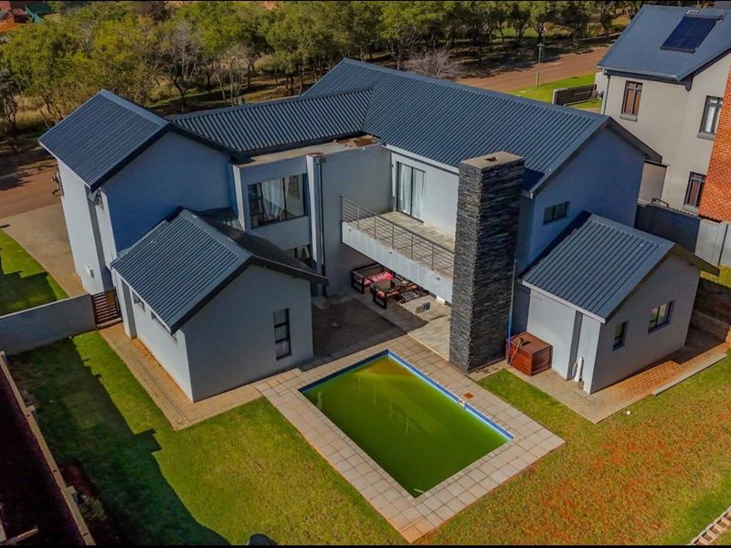 Aerial view of a modern double-story house featuring a metal roof, stone-clad chimney, balcony, and a swimming pool in the rear garden.