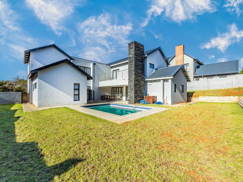 Rear view of the property featuring a swimming pool, stone-clad chimney, and a spacious garden with a paved patio area.