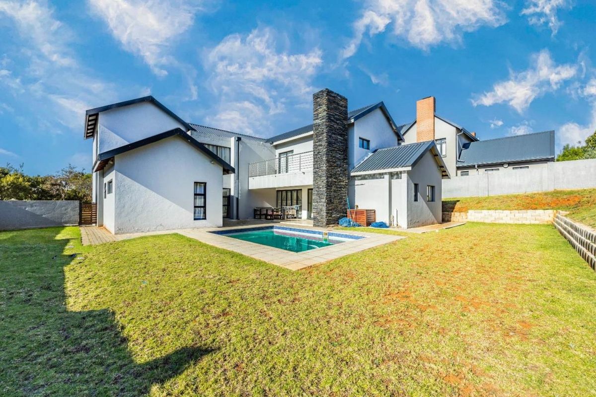 Rear view of the property featuring a swimming pool, stone-clad chimney, and a spacious garden with a paved patio area.
