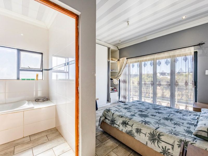 A spacious bedroom featuring built-in wardrobes, tiled flooring, and sliding glass doors leading to a balcony, with an adjoining en-suite bathroom area.