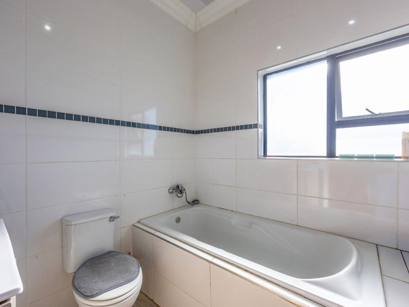 A functional bathroom featuring a built-in bathtub, toilet, and white wall tiling with a decorative accent border.