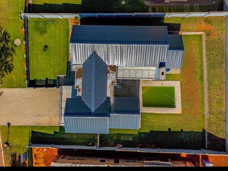 Aerial view of the property showing the house layout, metal roofing, swimming pool, surrounding garden, and perimeter boundary walls.