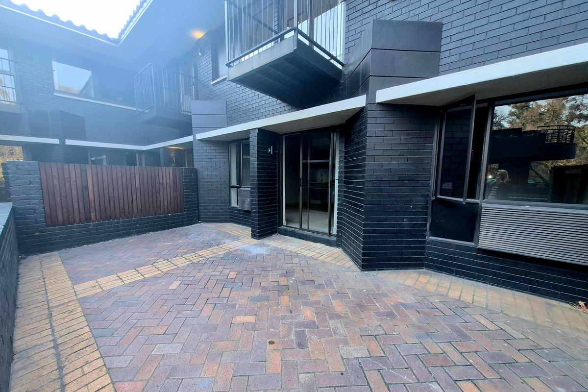 A private rear courtyard featuring dark brick exterior walls, paved flooring, and access to the apartment via a sliding glass door.