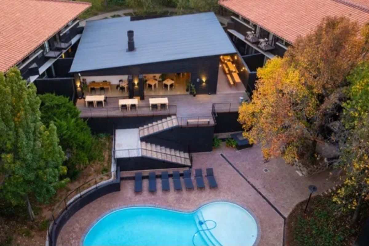Aerial view of an apartment complex featuring a central swimming pool, outdoor terrace, and modern dark-toned building architecture.