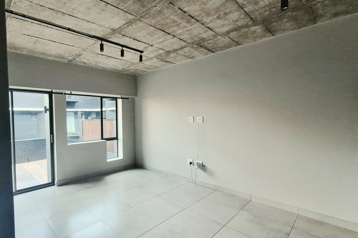 Modern, empty living area featuring an industrial-style exposed concrete ceiling, sleek track lighting, large format floor tiles, and access to an outdoor patio.