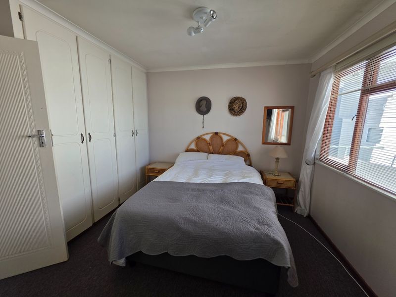 A functional bedroom featuring built-in cupboards, neutral wall finishes, and a window with blinds, offering a clean and practical living space.
