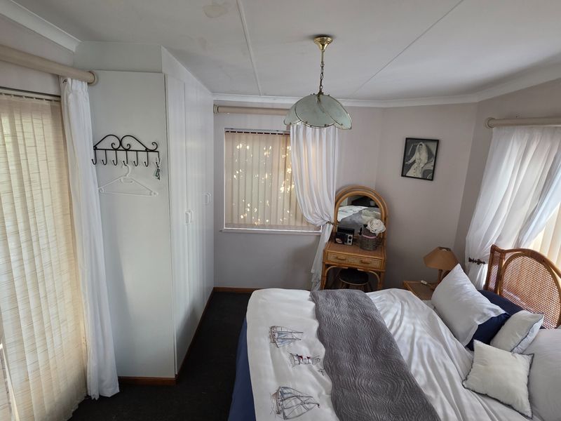 A bedroom featuring built-in wardrobes, vertical blinds, and a ceiling pendant light, with visible water staining on the ceiling.
