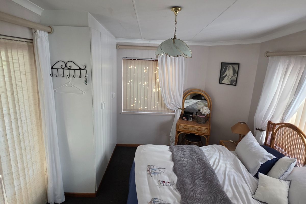 A bedroom featuring built-in wardrobes, vertical blinds, and a ceiling pendant light, with visible water staining on the ceiling.