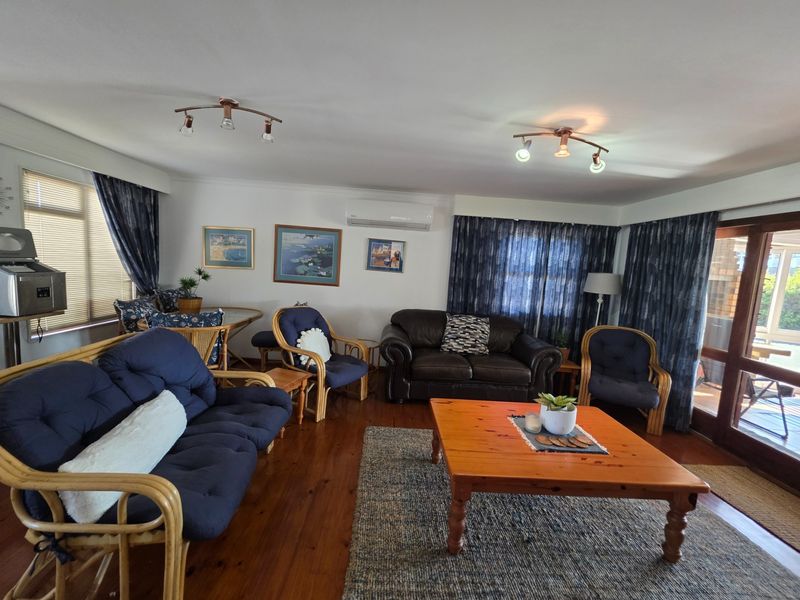 A spacious living room featuring polished hardwood flooring, split-system air conditioning, and direct access to an outdoor patio area through sliding glass doors.