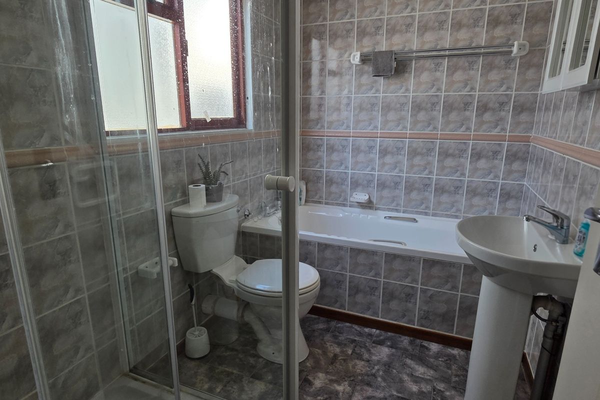 A functional bathroom featuring a pedestal basin, bathtub, and a separate shower enclosure with tiled finishes throughout.