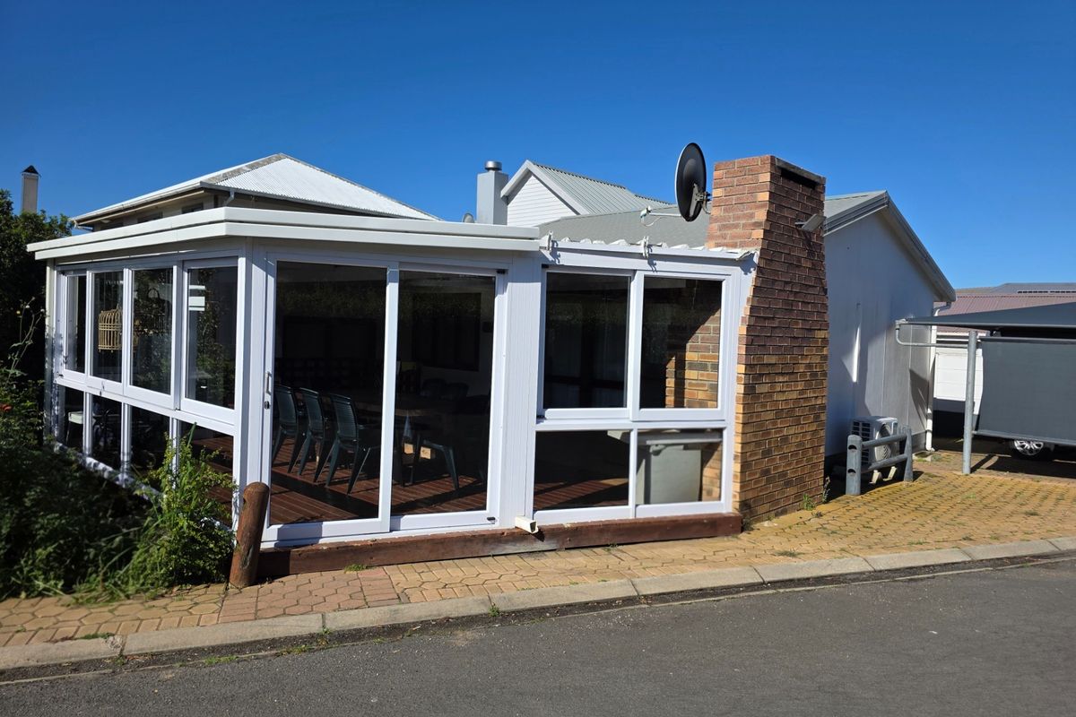 Rear view of the property featuring an enclosed patio with sliding glass doors, a brick chimney, and paved outdoor area.