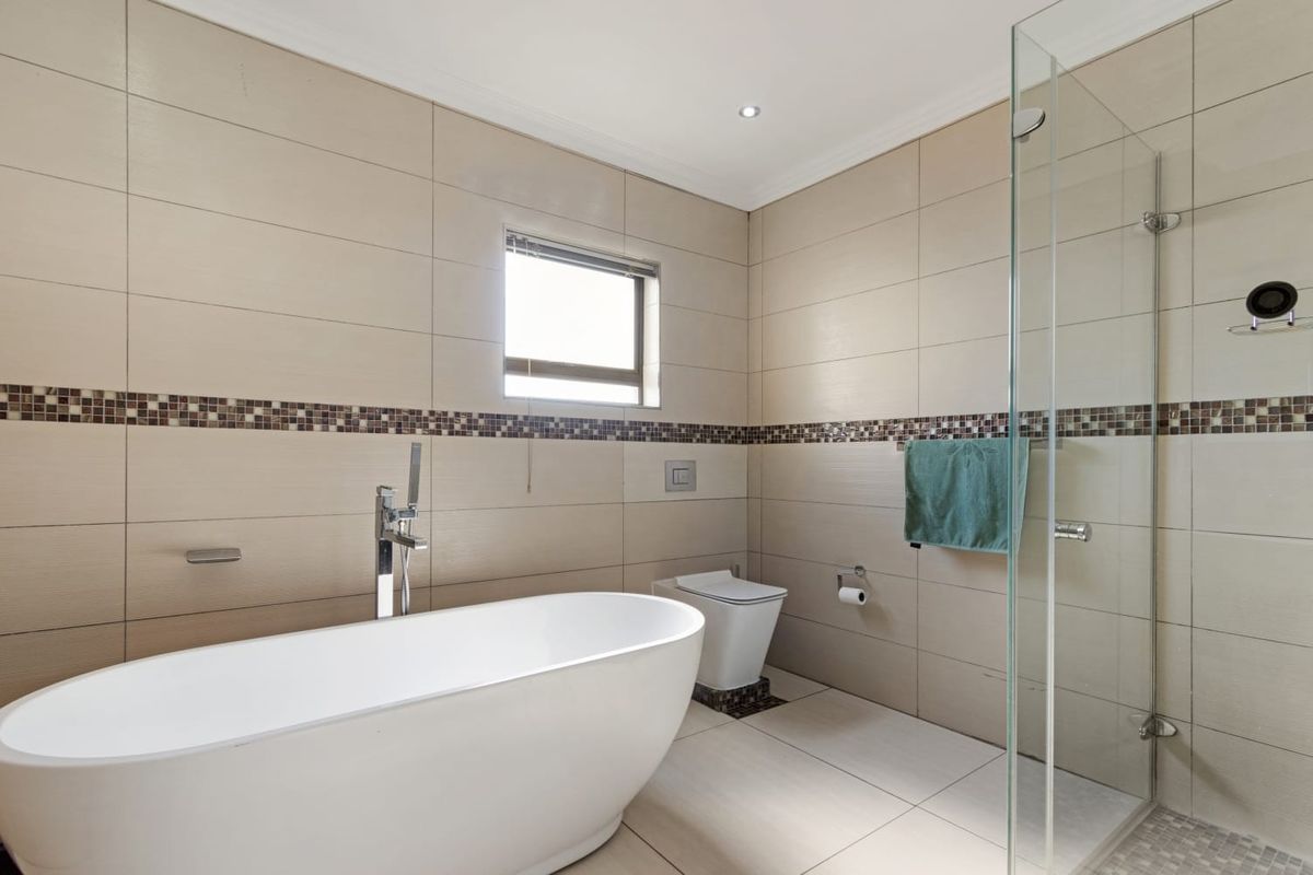 Modern bathroom featuring a sleek freestanding bathtub, wall-mounted toilet, and a glass-enclosed shower with neutral floor-to-ceiling tiling.