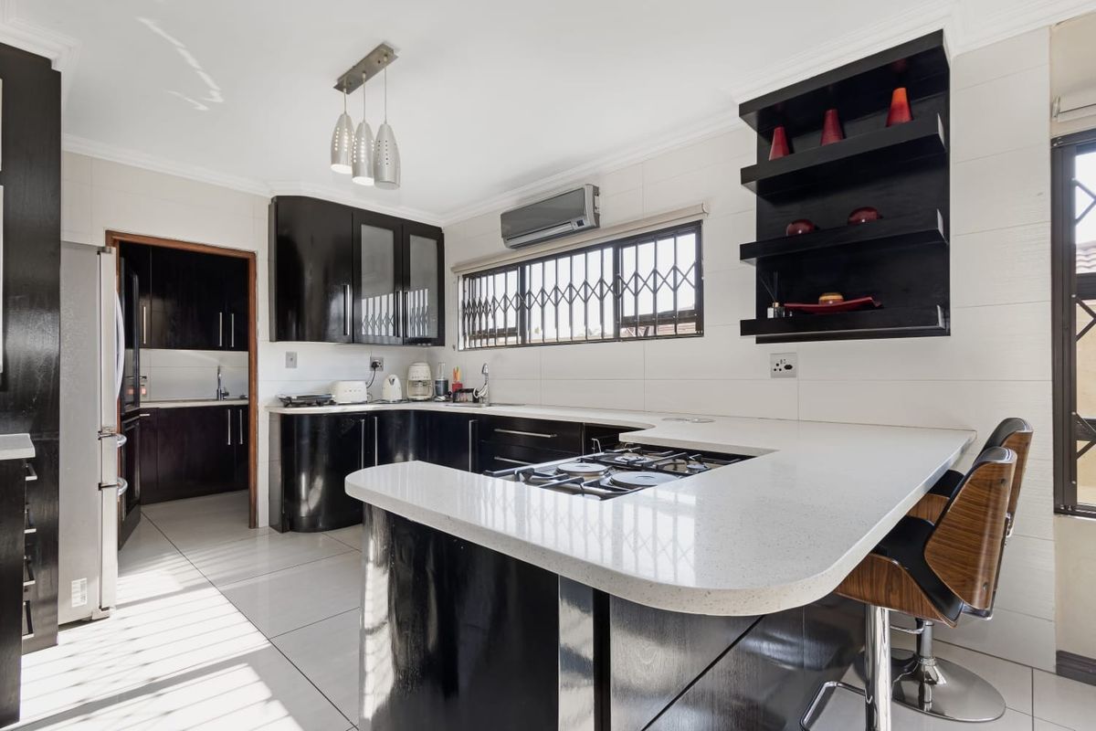 Modern kitchen featuring dark cabinetry, stone countertops, integrated gas hob, and tiled flooring, with an adjacent scullery area visible.