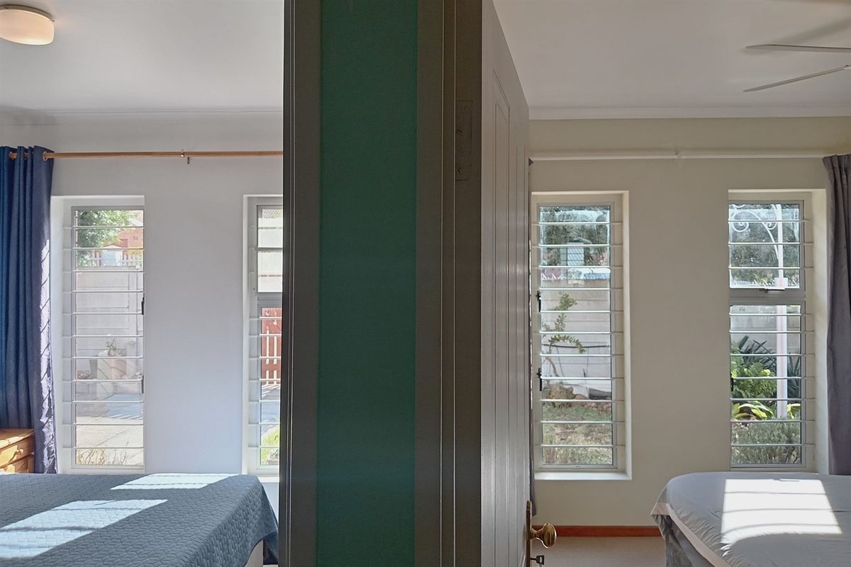 A bedroom featuring security bars on the windows and a ceiling fan, offering a functional layout with natural light.