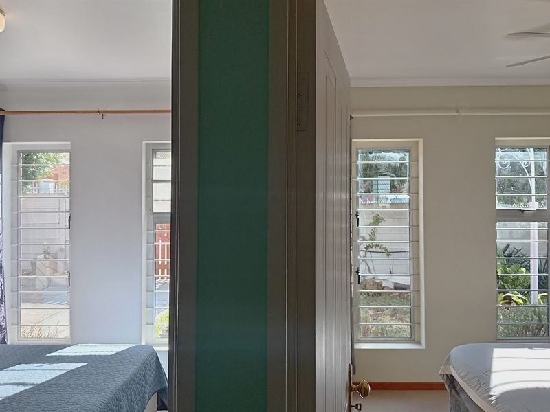 A bedroom featuring security bars on the windows and a ceiling fan, offering a functional layout with natural light.