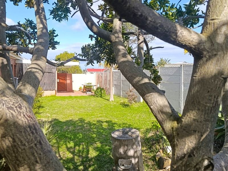 A private rear garden featuring a well-maintained lawn, paved patio area, and secure perimeter walling, viewed through mature trees.