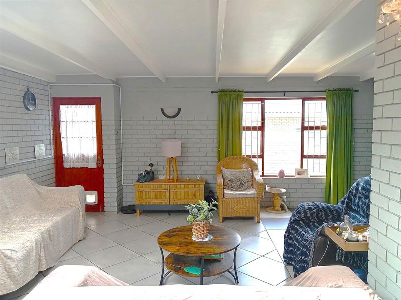 A living room featuring painted brick walls, tiled flooring, and exposed beam ceilings, offering a functional space with natural light through security-barred windows.