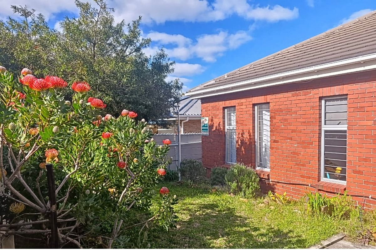 A view of the rear exterior featuring a face brick facade, tiled roof, and secure aluminium-framed windows overlooking a garden area.