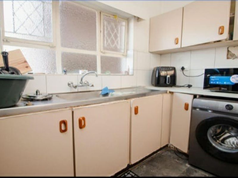 A functional kitchen featuring laminate cabinetry, a stainless steel sink, and tiled splashbacks, requiring cosmetic updates to modernize the space.