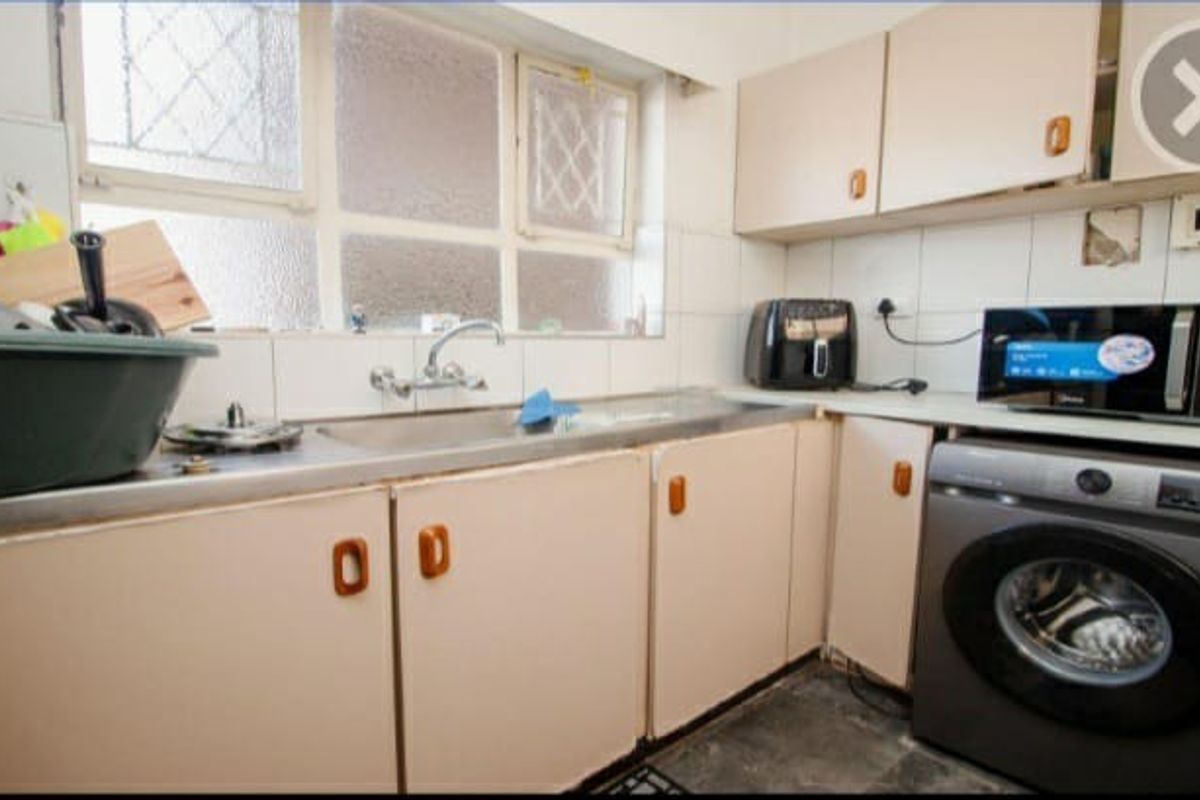 A functional kitchen featuring laminate cabinetry, a stainless steel sink, and tiled splashbacks, requiring cosmetic updates to modernize the space.