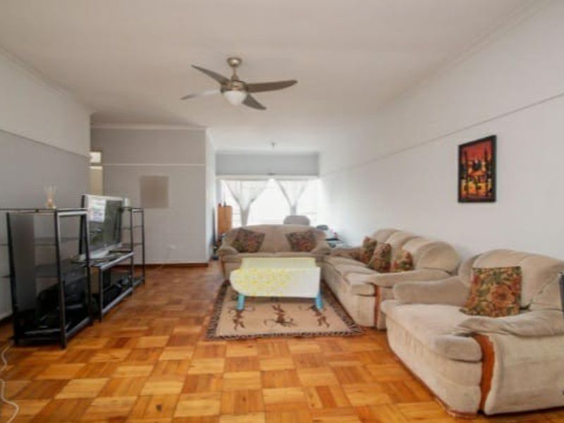 Spacious living room featuring classic parquet flooring, a ceiling fan, and traditional picture rails, offering a versatile layout for comfortable seating arrangements.
