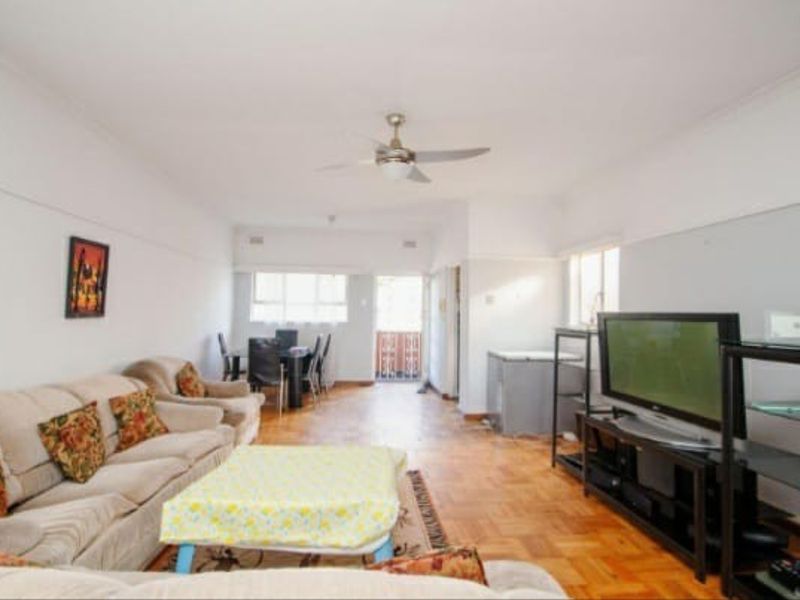 Spacious open-plan living and dining area featuring classic parquet flooring, a ceiling fan, and access to an outdoor balcony.