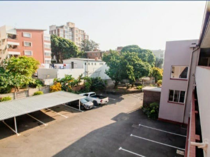An elevated view of the apartment complex rear exterior, featuring a paved parking area with covered carports and a balcony walkway.