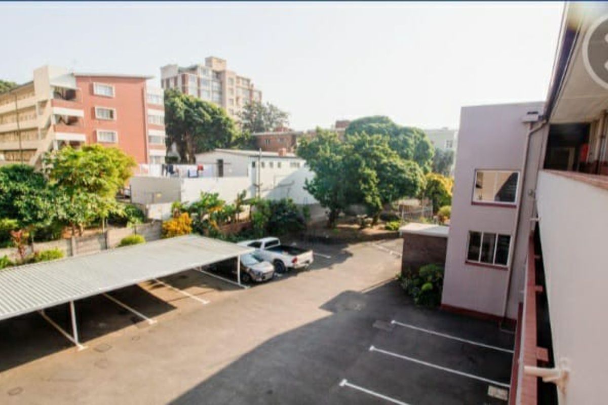 An elevated view of the apartment complex rear exterior, featuring a paved parking area with covered carports and a balcony walkway.