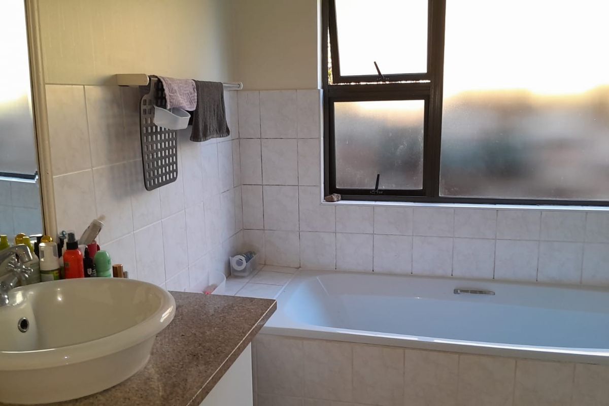 A functional bathroom featuring a built-in bathtub, vanity basin, and tiled splashback, offering a practical layout with natural light from a top-hung window.