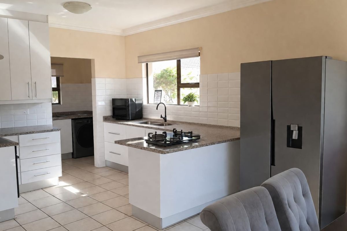 A well-maintained kitchen featuring white cabinetry, granite countertops, a gas hob, and an adjoining scullery area with tiled flooring throughout.