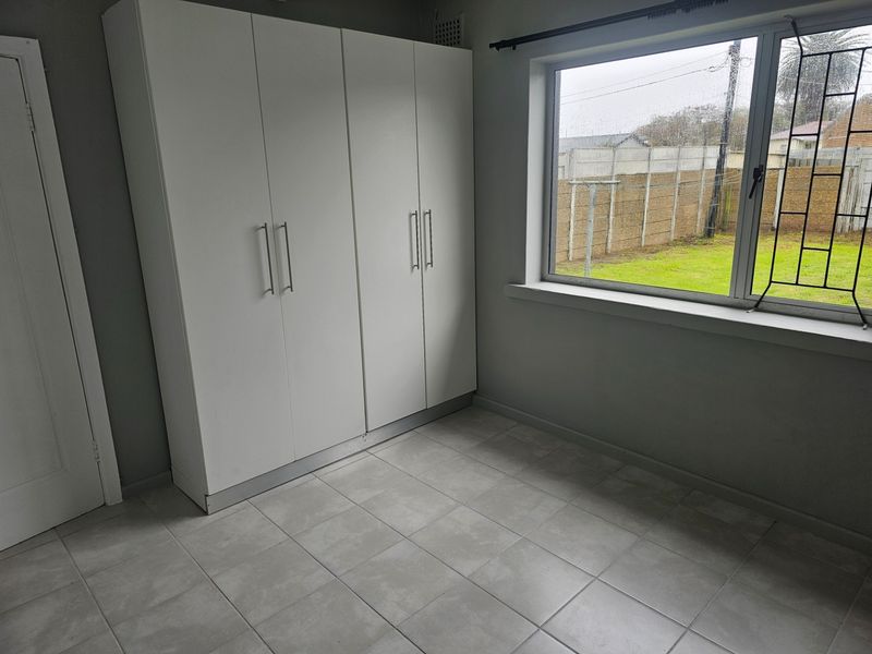 A clean, empty bedroom featuring neutral tiled flooring and a modern white built-in wardrobe with ample storage space.