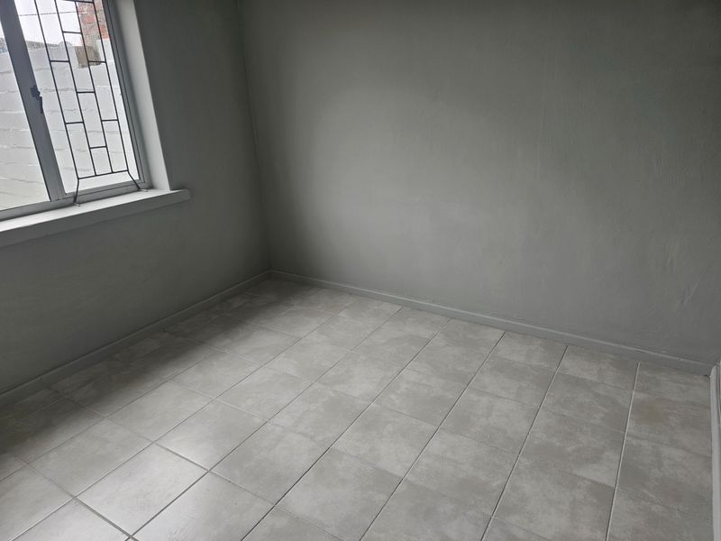 A clean, empty bedroom featuring neutral grey tiled flooring and a window fitted with security bars.