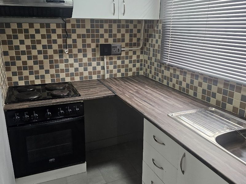 Compact kitchen featuring white cabinetry, wood-look laminate countertops, a built-in electric stove with extractor fan, and a tiled backsplash.