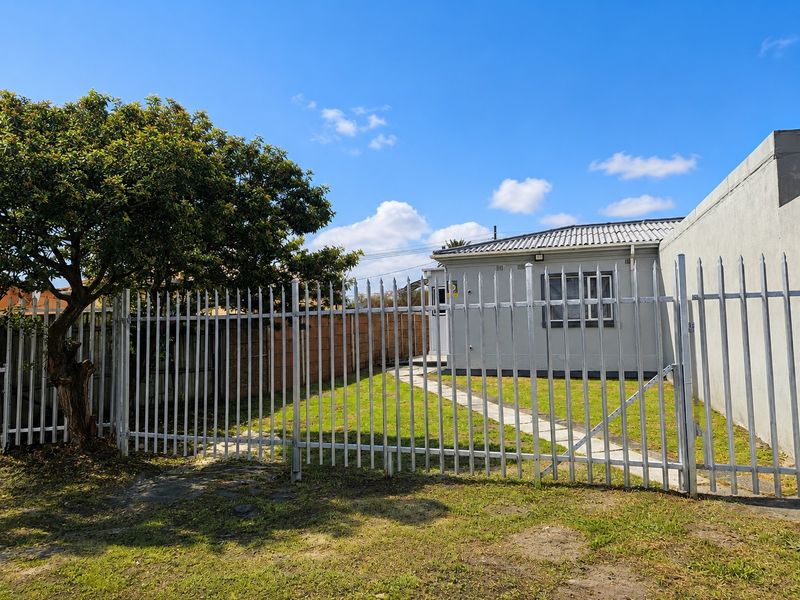 Rear view of the townhouse featuring a private garden, paved pathway, and secure metal perimeter fencing.