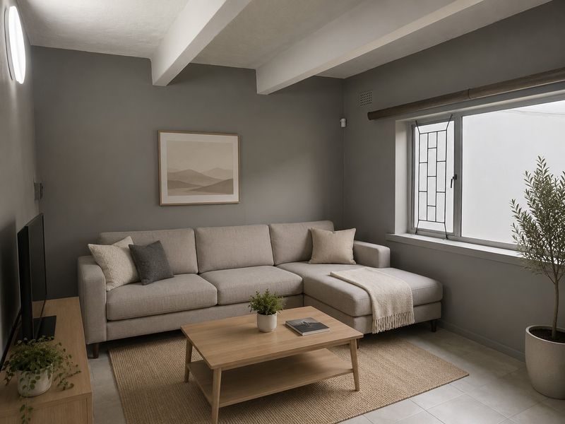 A well-maintained living room featuring exposed ceiling beams, neutral grey walls, and tiled flooring, providing a clean and contemporary living space.