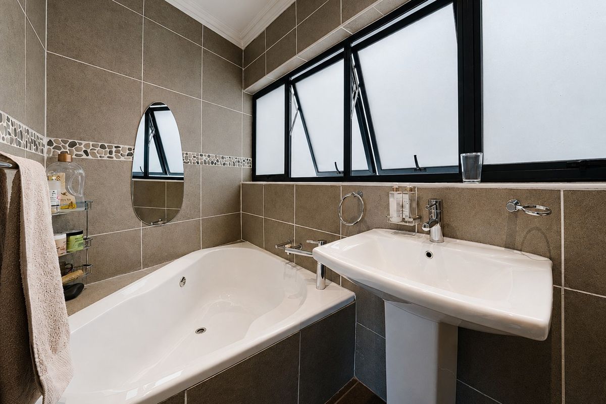 A well-maintained bathroom featuring a built-in bathtub, pedestal basin, and modern tiled finishes with frosted glass windows for privacy.