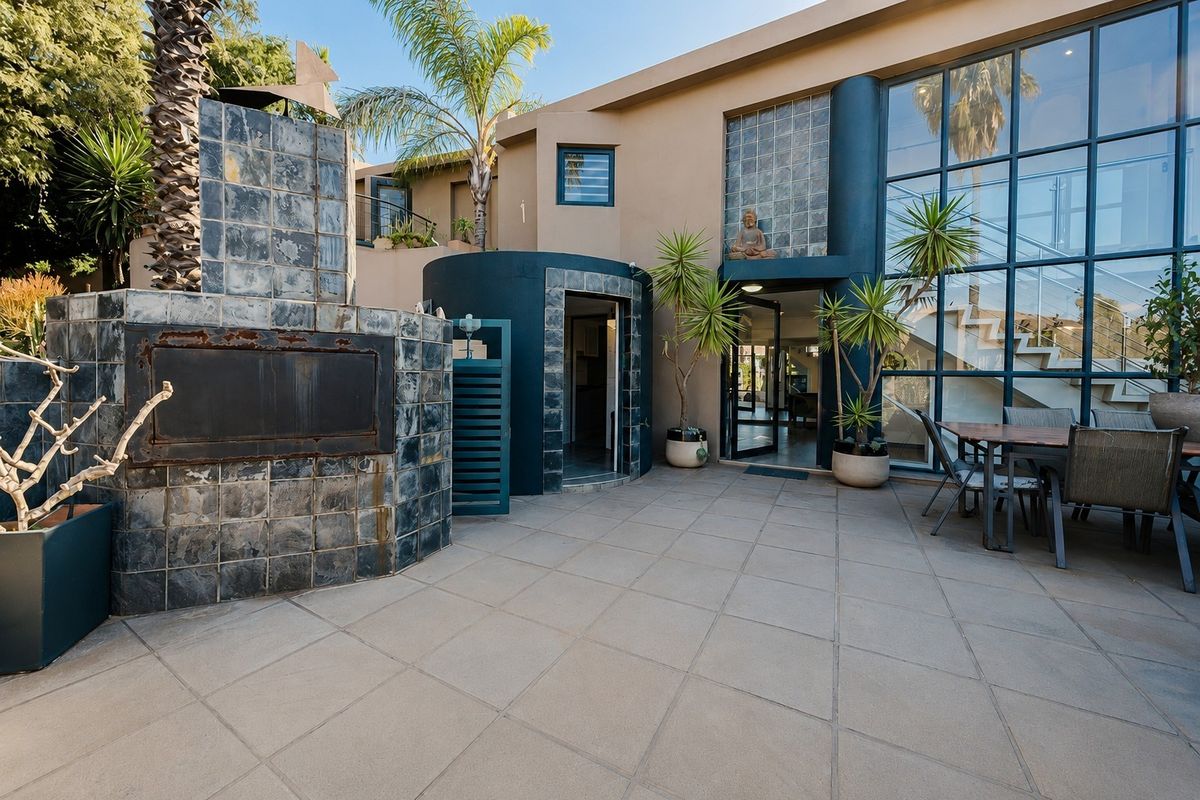 Spacious outdoor patio featuring a built-in tiled fireplace, large glass curtain wall, and direct access to the interior living space.